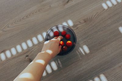 Cropped image of hand picking cherry tomatoes from bowl on wooden table