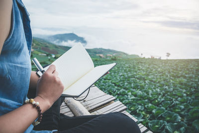 Midsection of woman reading book against landscape