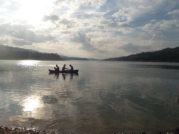 People traveling on boat in lake against sky