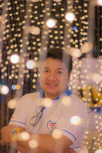 Portrait of mid adult man standing against illuminated lighting equipment