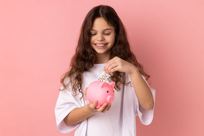 Portrait of young woman with arms raised against pink background