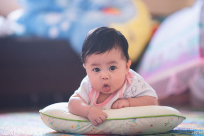 Portrait of cute baby girl sticking out tongue while lying on pillow at home