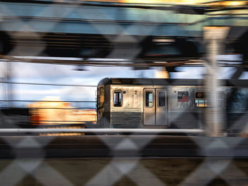 View of nyc subway car as it speeds up across the manhattan bridge through chain link fence 