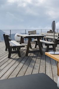 Empty chairs and table at beach against sky