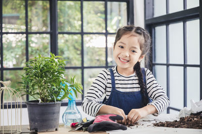 Portrait of cute girl gardening on table with potted plant indoors