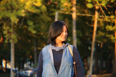 Thoughtful mature woman standing against trees during sunset