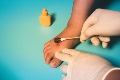 Cropped hands of person cleaning wound with cotton swab against blue background