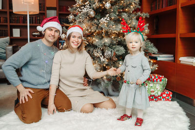 Portrait of cheerful family sitting by christmas tree