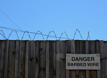 Warning sign on fence against clear blue sky