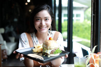 Portrait of smiling young woman holding fast food in restaurant