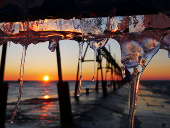 Close-up of icicles on beach against sky during sunset
