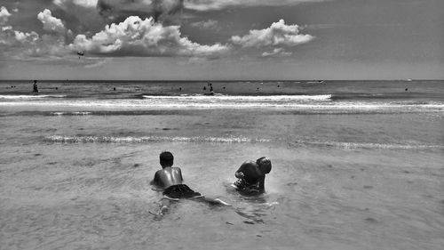 Playful shirtless boys at beach against sky