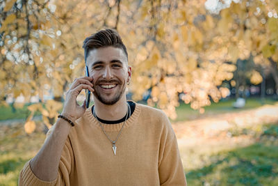Young man using smart phone while standing on tree