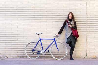 Young woman leaning on a city wall with vintage bike in sunny day