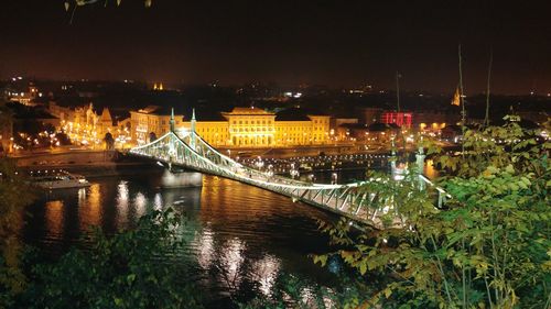 Illuminated bridge over river in city at night