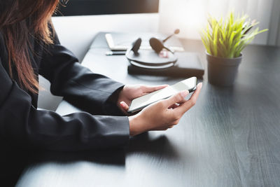 Midsection of woman using mobile phone while sitting on table