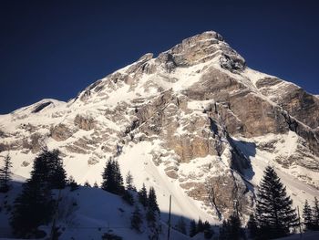 Low angle view of snowcapped mountains against clear blue sky