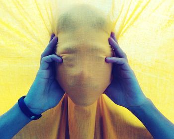 Cropped hands holding mask behind yellow curtain