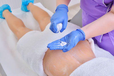 Midsection of nurse spraying cream for applying on patient in hospital