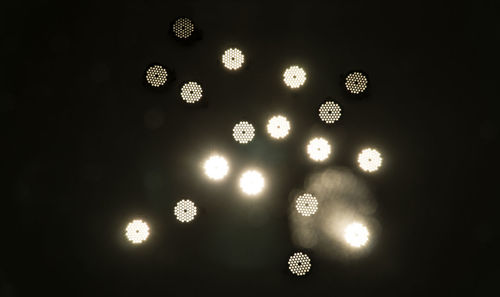 Low angle view of illuminated lighting equipment against black background