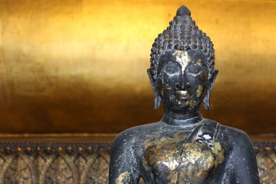 Close-up of old buddha statue against golden wall