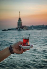 Midsection of man holding ice cream against sky during sunset