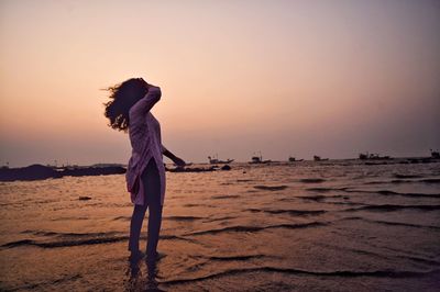 Side view of woman standing at beach against sky during sunset