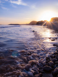 Sunset sunflare on a beach with water glistening over rocks