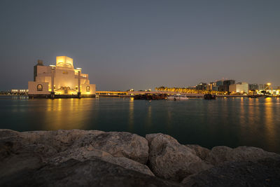 Illuminated buildings by sea against sky at night