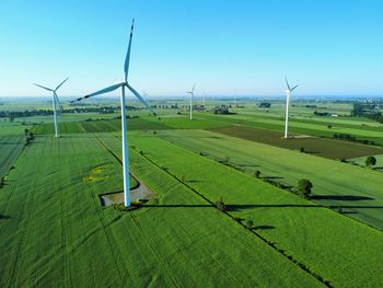 Windmills on field against clear blue sky