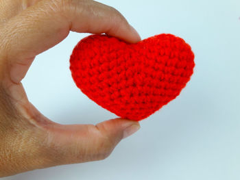 Close-up of hand holding red heart shape over white background