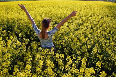 Rear view of woman with arms raised standing in field