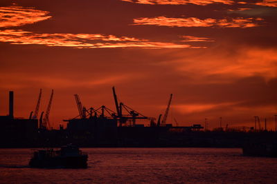 Silhouette cranes at commercial dock against sky during sunset