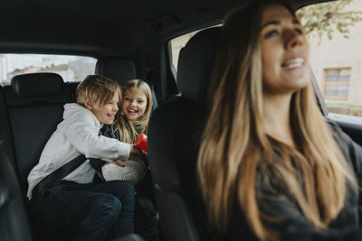 Happy brother and sisters sitting behind while mother driving car on weekend