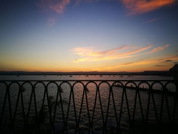 Silhouette railing by sea against sky during sunset