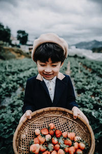 Boy holding basket with strawberries at farm