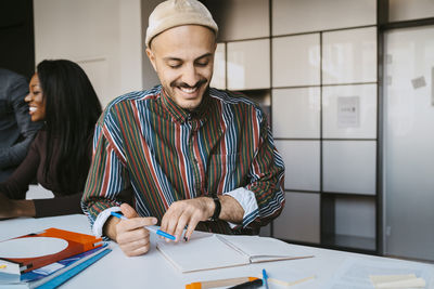 Smiling male student reading book while leaning on table at community college