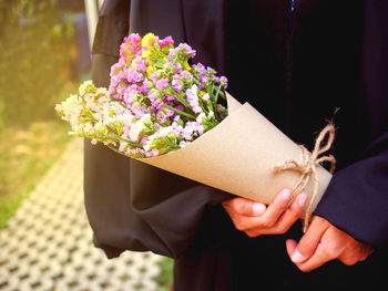 Midsection of person in graduation gown with flower bouquet