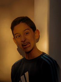 Boy making a face while standing against wall at home