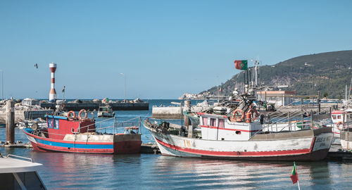 Boats moored at harbor against clear blue sky