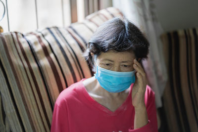 Close-up of senior woman wearing mask sitting at home