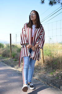 Full length portrait of young woman standing against sky