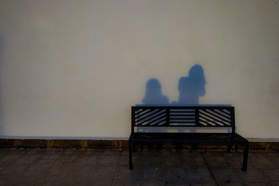 Rear view of people sitting on bench against wall