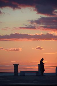 Silhouette people standing by railing against sky during sunset