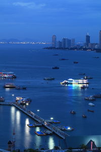 Aerial view of illuminated city by sea against sky at dusk