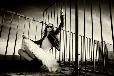 A ballerina in tutu sitting at the fence on the roof at sunset in boots and a jacket