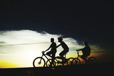 Silhouette people riding bicycles against sky during sunset