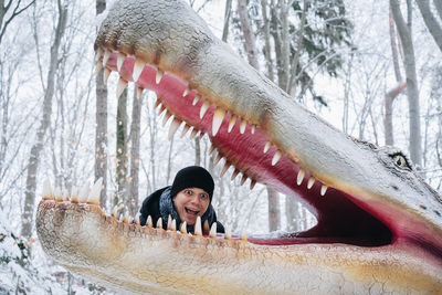 Portrait of mid adult man standing by dinosaur sculpture in forest during winter