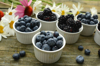 Blueberries and blackberries in small white ramekins with garden daisies on rustic wood table