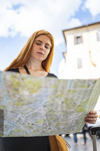 Red hair woman in a city looking at paper map with blue sky backgroung